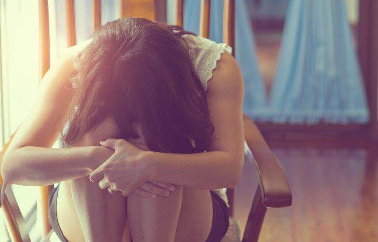Depressive Frau sitzt zusammengekauert in einem Stuhl