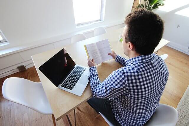 Ein Mann liest ein Buch, während er am Laptop arbeiten sollte
