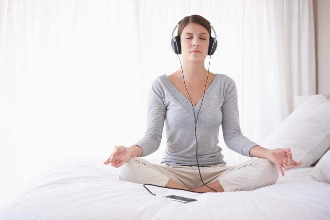 Eine Frau trägt Kopfhörer beim Meditieren im Bett