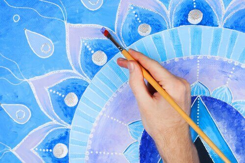 Eine Hand malt ein Mandala in blauen Tönen aus