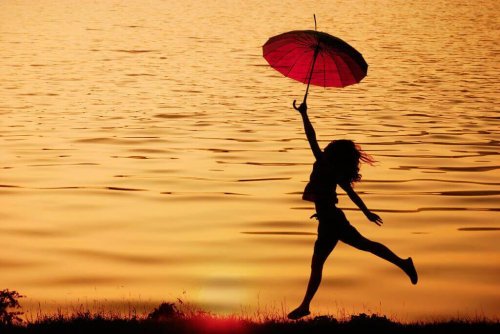 Frau, die glücklich und motiviert mit einem Regenschirm beim Sonnenuntergang tanzt.