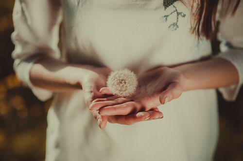 Frau trägt Pusteblume auf der Hand