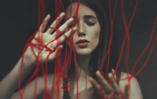 Eine Frau hat sich in einem roten Faden verhängt, der häusliche Gewalt und Missbrauch symbolisiert, aus denen wir uns nur schwer losreißen können.