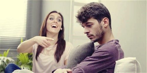 Eine Frau sitzt neben ihrem Freund und lacht ihn höhnisch aus.