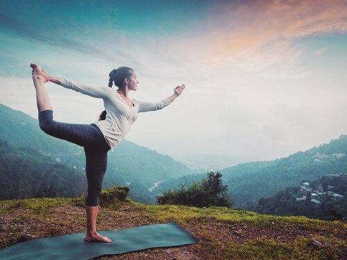 Eine Frau praktiziert auf einer Matte in der Natur Yoga.