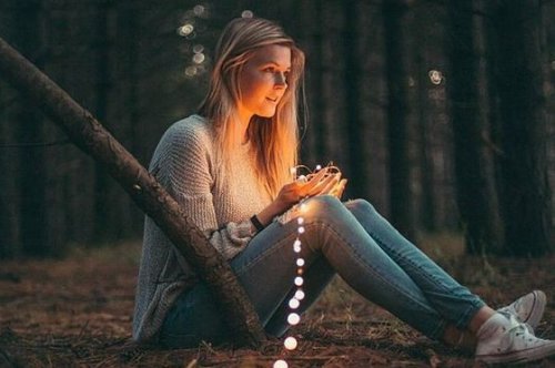 Eine im Wald sitzende Frau hält eine Lichterkette. Dabei denkt sie über die Lösung tief sitzender Konflikte nach.
