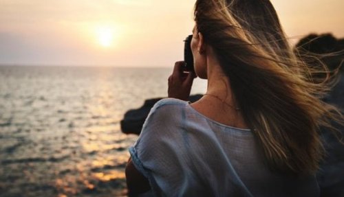 Eine Frau macht ein Foto vom Sonnenuntergang über dem Meer.