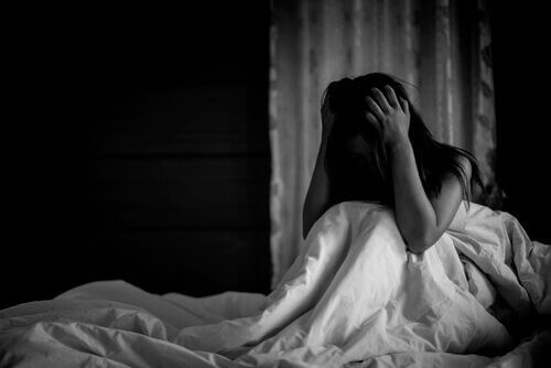 Panikattacken in der Nacht - Eine Frau sitzt aufrecht im Bett und scheint von einer Panikattacke gepeinigt zu sein.