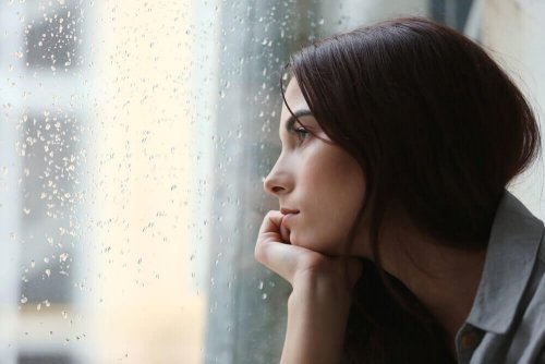 Frau schaut mit trauriger Miene aus dem Fenster