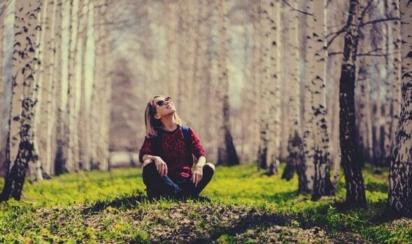 Frau sitzt im Wald und schaut in den Himmel
