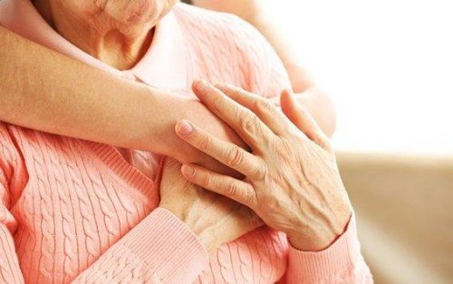 Niedergeschlagenheit bei Senioren begegnen - Eine junge Frau umarmt eine ältere Frau von hinten, ihre Hände liegen aufeinander.