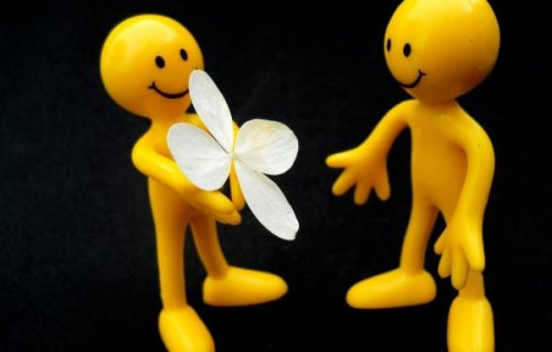 Eine gelbe Figur gibt einer anderen gelben Figur eine Blüte. 
