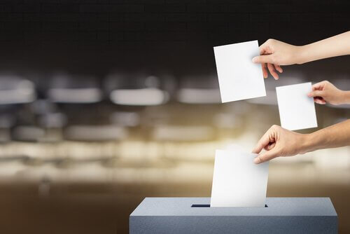 Drei Hände mit Wahlzetteln über einer Wahlurne