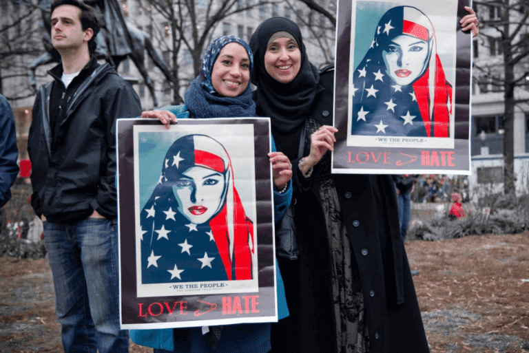 Zwei muslimische Frauen halten stolz Plakate gegen Fremdenfeindlichkeit hoch.