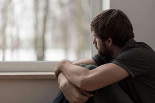 Kauernder Mann schaut aus dem Fenster und steht als Symbol für negative Einsamkeit
