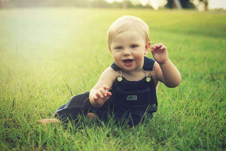 Kleinkind sitzt auf dem Rasen und lacht