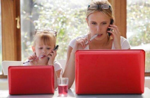 Ein Mädchen starrt in einen Laptop, mit einer Brille auf dem Kopf, Stift im Mund und Handy am Ohr und imitiert damit exakt die Frau neben ihr.