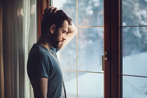 Mann mit Hand auf dem Kopf steht vor einem Fenster in Winterlandschaft