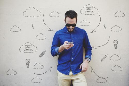 Neue Arten der Kommunikation: Ein Mann starrt auf sein Handy; auf der weißen Wand hinter ihm sind kleine Zeichnungen dargestellt, unter anderem Gedankenblasen oder eine Glühbirne.