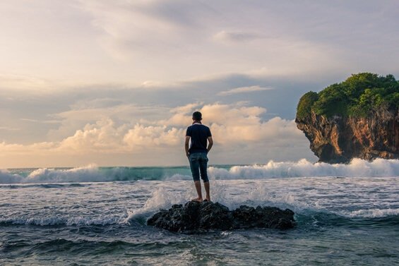 Mann steht auf einem Felsen im Meer