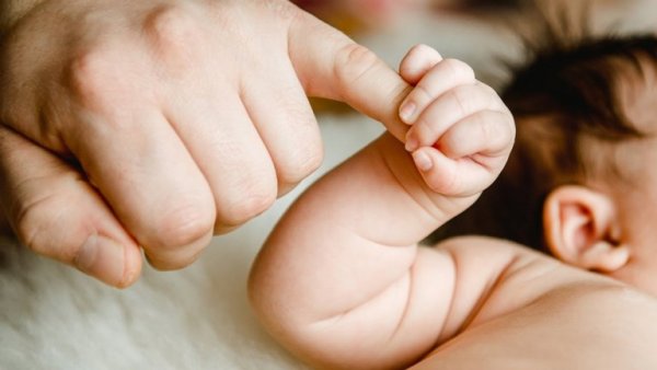Eine Baby hält sich am Finger eines Erwachsenen fest.
