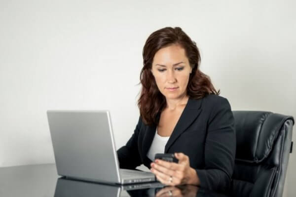 Präsentismus symbolisiert durch eine Frau, die gerade am Laptop arbeitet und auf ihr Smartphone schaut