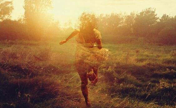 Frau rennt auf einem Feldweg in Richtung Sonne