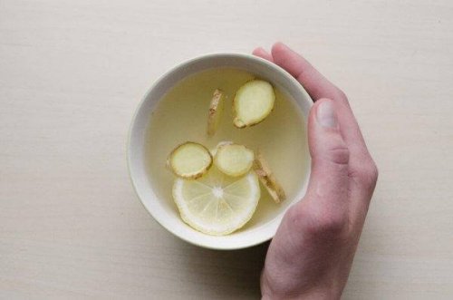 Eine Hand ist um eine Tasse Tee gelegt, der mit Ingwer und Zitrone gemacht ist.