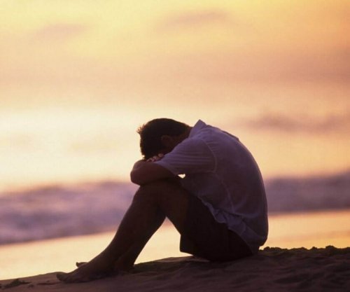 Ein Mann sitzt am Meer und hat seinen Kopf auf seine Knie gelegt.