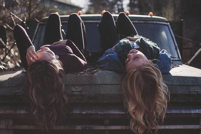Zwei Freundinnen liegen auf einem Auto und schauen lachend in den Himmel