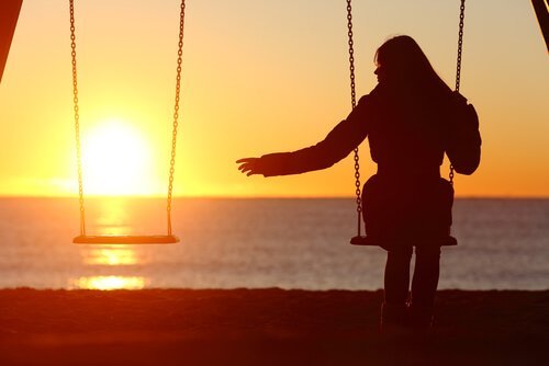 Einsame Frau sitzt allein auf einer Schaukel; die Schaukel neben ihr bleibt leer