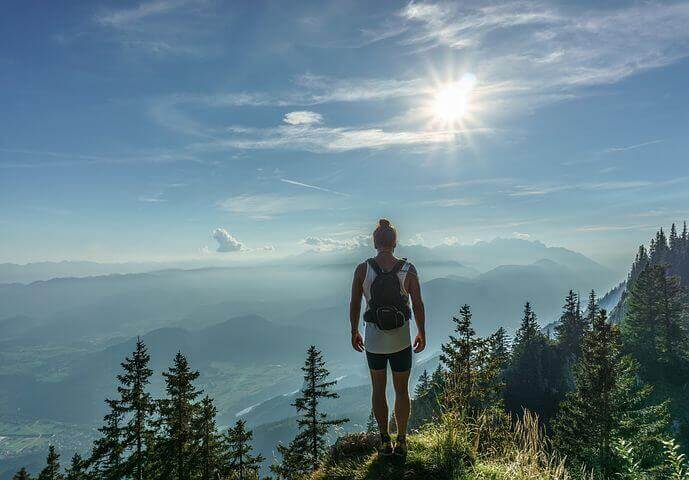 Ein Mensch steht auf einem Berggipfel und blickt in ein Tal.