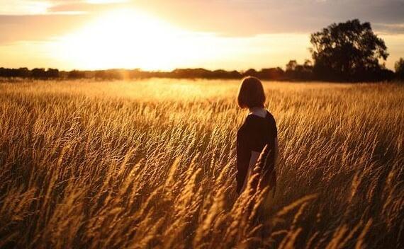 Frau steht bei Sonnenuntergang auf einem Feld