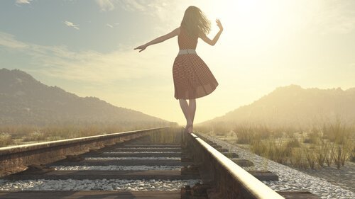 Eine Frau im Kleid balanciert auf einem Bahngleis.