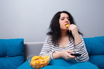 Sitzender Lebensstil - Dicke Frau auf dem Sofa isst Chips 