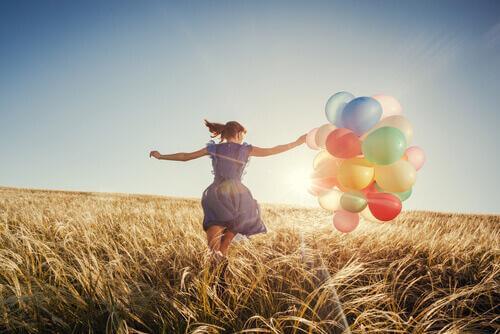 Eine junge Frau läuft mit bunten Ballons über ein Getreidefeld.