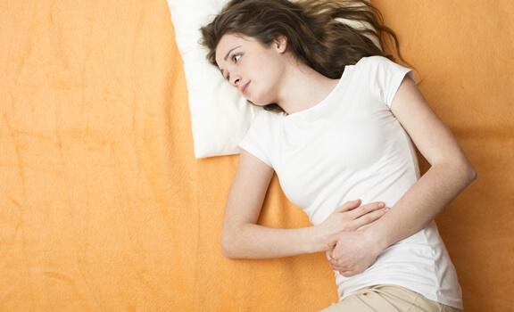 Frau liegt mit Bauchschmerzen im Bett