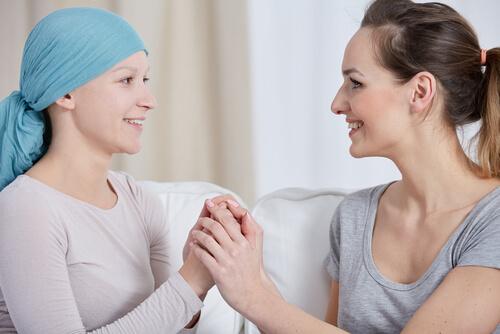 Eine Frau hält die Hand einer an Krebs erkrankten Frau; sie lächeln sich beide an.