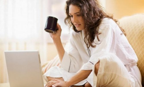 Eine Frau hält eine Tasse in ihrer rechten Hand, während sie mit der linken Hand auf ihrem Laptop tippt.