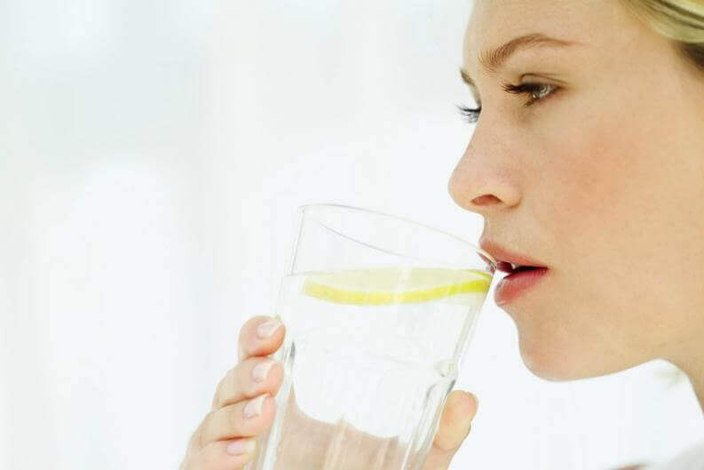 Frau trinkt Wasser mit einer Scheibe Zitrone