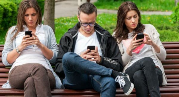 Freunde sitzen zusammen auf einer Parkbank und schauen gleichzeitig auf ihre Handys. 
