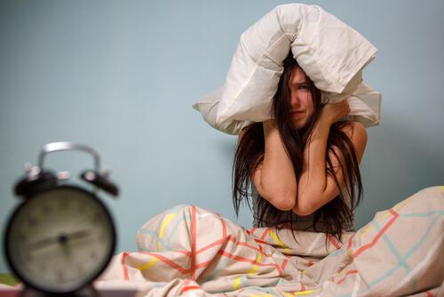 Eine frustrierte Frau zieht sich ein Kissen über den Kopf. 