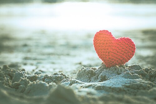 Ein rotes Herz steckt im Sand.