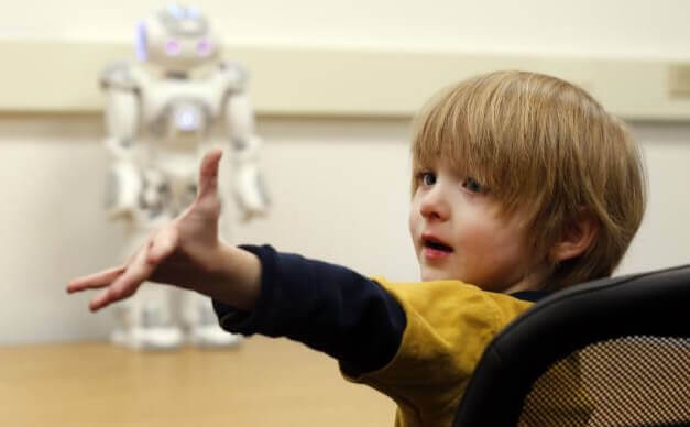 Ein Junge streckt seine Hand aus, im Hintergrund wartet ein Roboter auf seinen Einsatz.