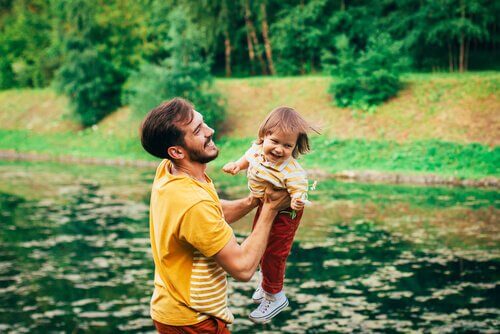 Vater hebt sein lachendes Kind vor einem See hoch