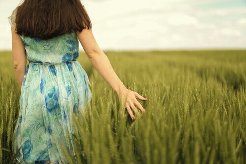 Eine Frau geht durch ein grünes Getreidefeld.