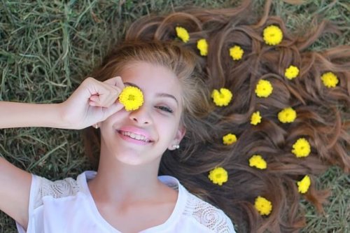 Mädchen hält eine gelbe Blume vor ihr Auge.