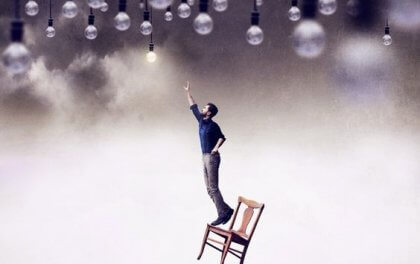 Ein Mann balanciert auf einem Stuhl und versucht, eine Glühbirne zu erreichen.