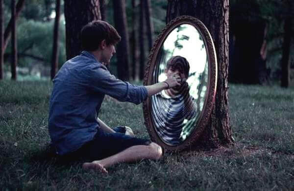 Mann sitzt in einem Wald auf dem Boden und blickt in einen Spiegel