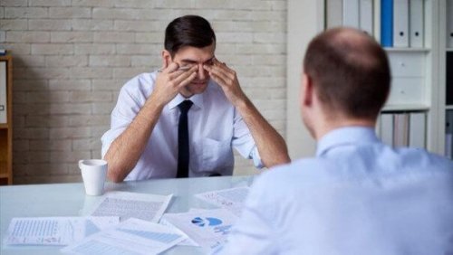 Ein Mann reibt sich im Büro müde die Augen.